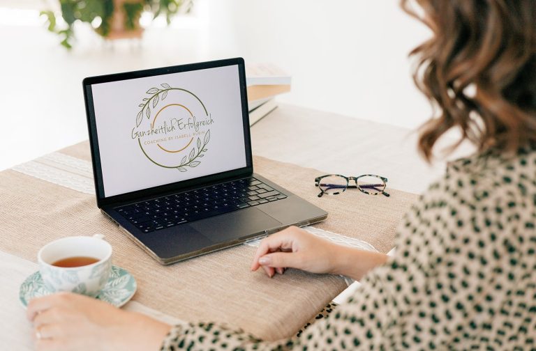 Kostenloses Kennenlerngespräch für ganzheitliches Life Coaching Frau sitzt an einem Tisch mit Laptop und Tasse Tee, schaut auf ein Logo-Design.