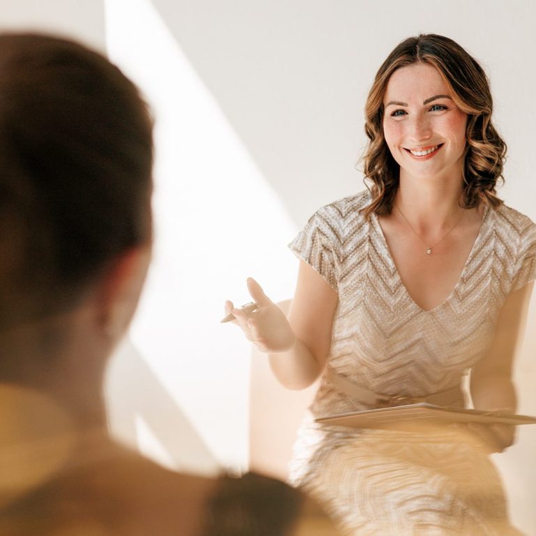 Ganzheitliches Coaching für gesunde Lebensführung in allen Bereichen Lächelnde Frau in eleganter Kleidung, die einer anderen Person gegenüber sitzt und spricht.